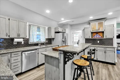 a kitchen with granite countertop a stove a sink dishwasher a dining table and chairs with wooden floor