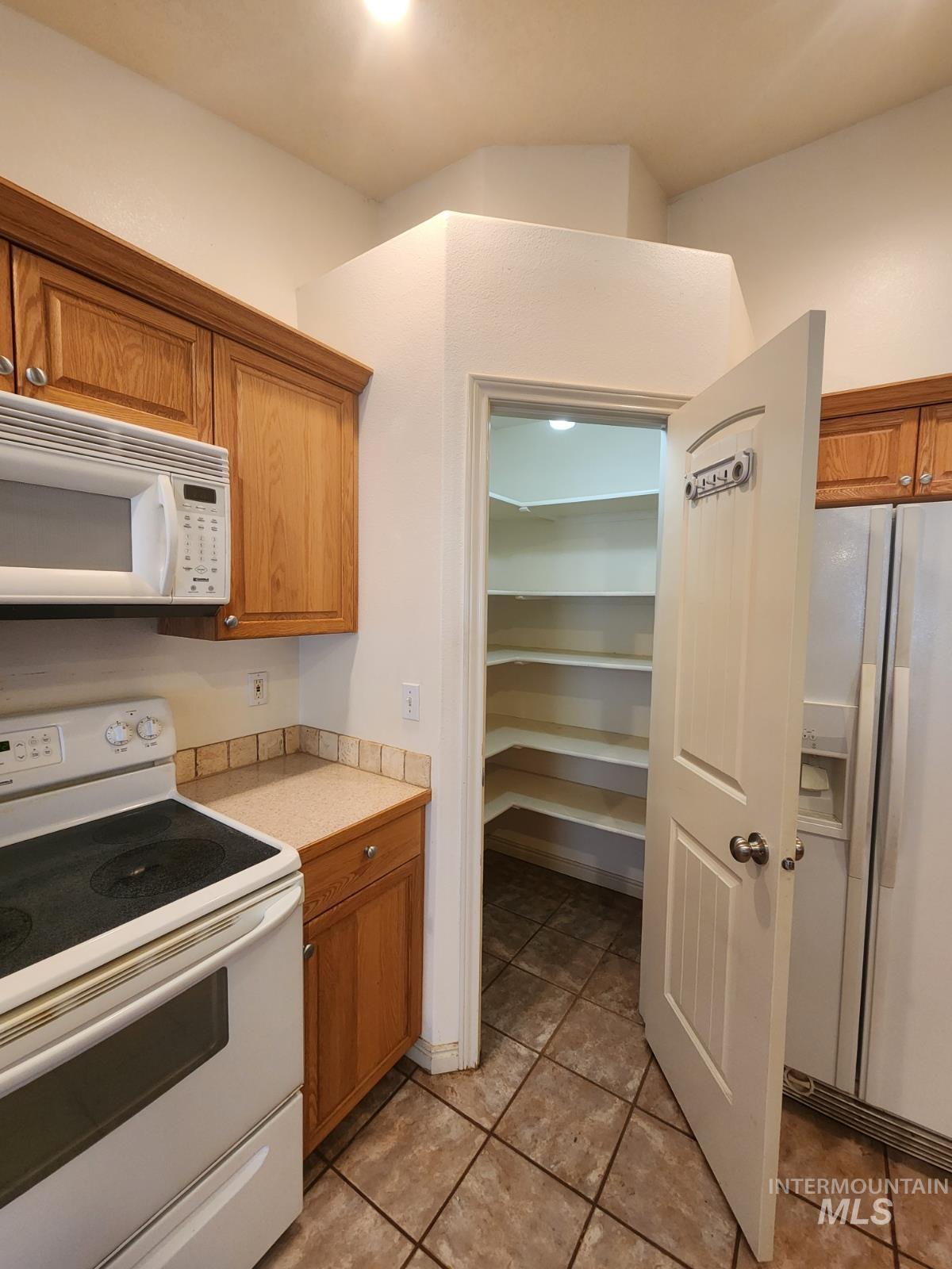 1000 North Rodeo Street Parma, ID 83660 - Photo 8 of 35 Kitchen featuring white appliances, light countertops, wood finish cabinetry, and light tile patterned floors