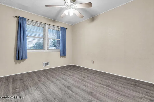 an empty room with wooden floor fan and windows