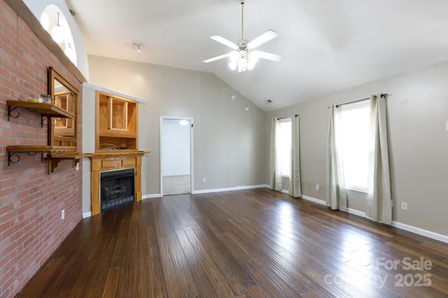 a view of an empty room with wooden floor fireplace and a window
