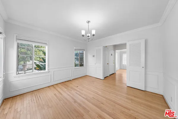 an empty room with wooden floor chandelier and windows