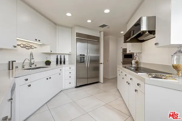 a kitchen with granite countertop a refrigerator oven a sink dishwasher and white cabinets with wooden floor