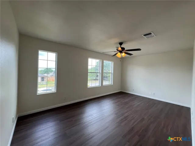 an empty room with wooden floor chandelier fan and windows