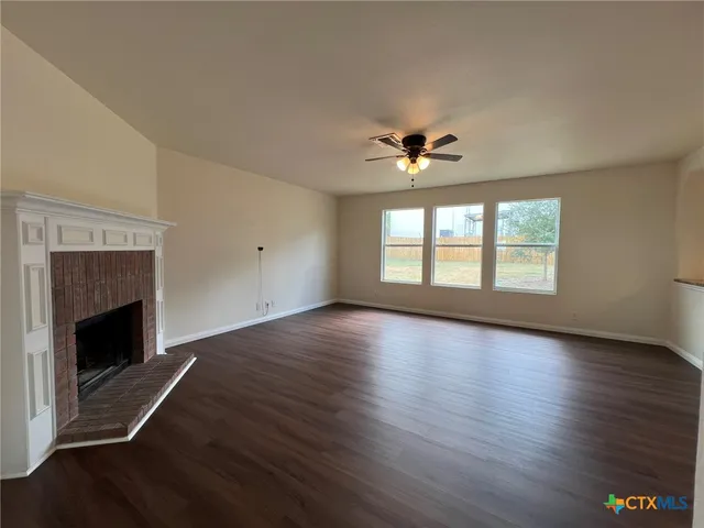 an empty room with wooden floor fireplace and windows