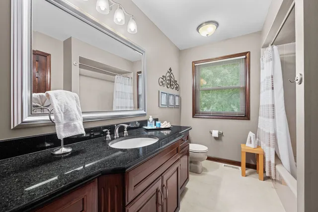 a bathroom with a granite countertop sink a toilet a mirror and a window