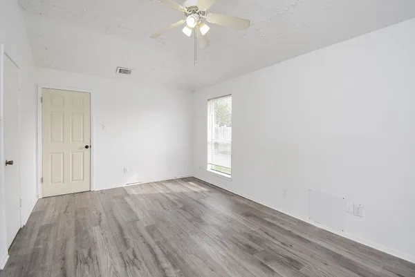 a view of an empty room with wooden floor and a ceiling fan