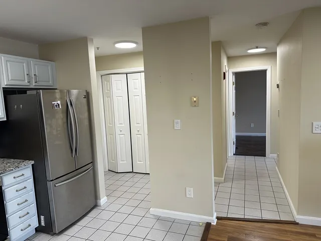 a view of a refrigerator in kitchen and an empty room in wooden floor