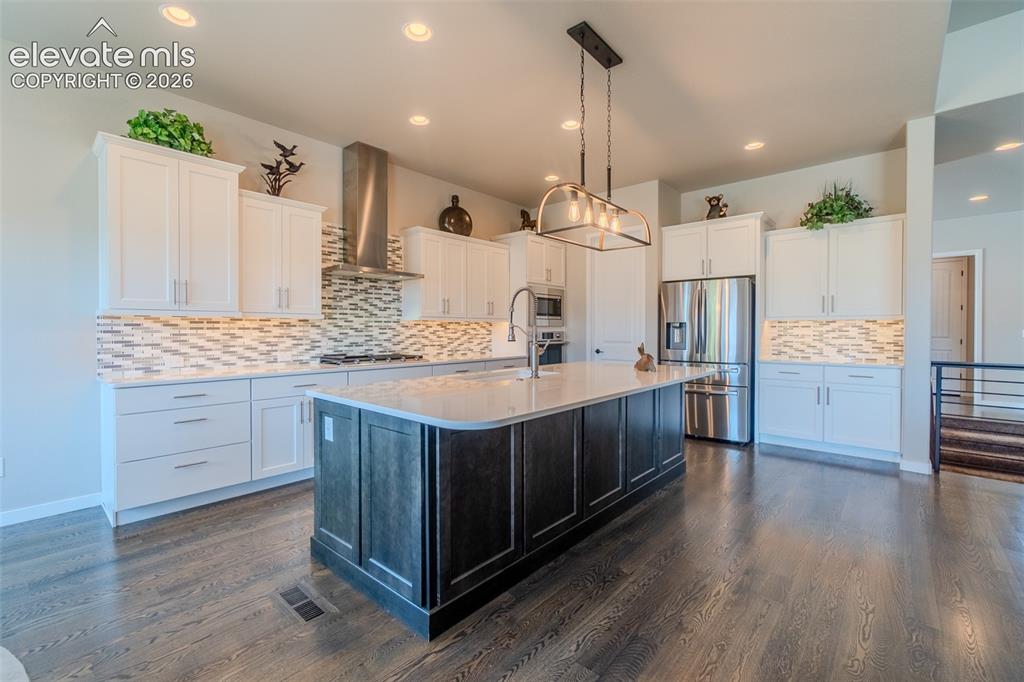 1061 Native Dancer Terrace Colorado Springs, CO 80921 - Photo 10 of 50 Spacious kitchen featuring an oversized island with a light-toned countertop, stainless steel appliances, white cabinetry, a tiled backsplash, and wood-finish flooring