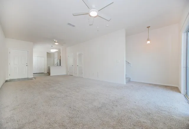 an empty room with a ceiling fan and kitchen view