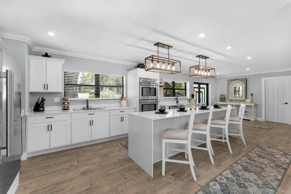 a large white kitchen with a stove top oven a sink dishwasher and a refrigerator with wooden floor