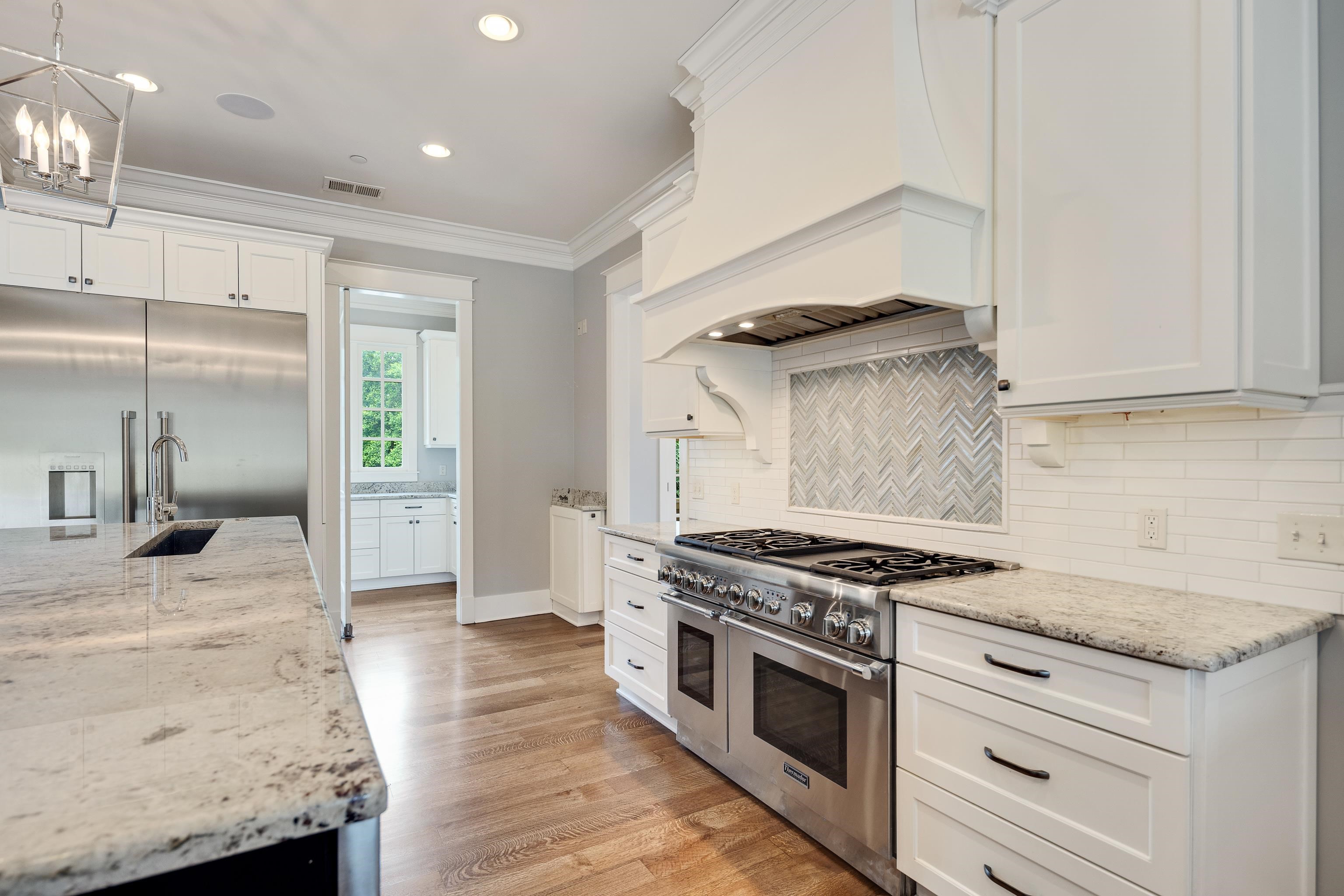 55 East Old State Line Road Piperton, TN 38017 - Photo 12 of 40 Gourmet kitchen featuring a professional-grade stainless steel range, white shaker cabinetry, patterned tile backsplash, substantial island with an undermount sink, and wood-finish flooring