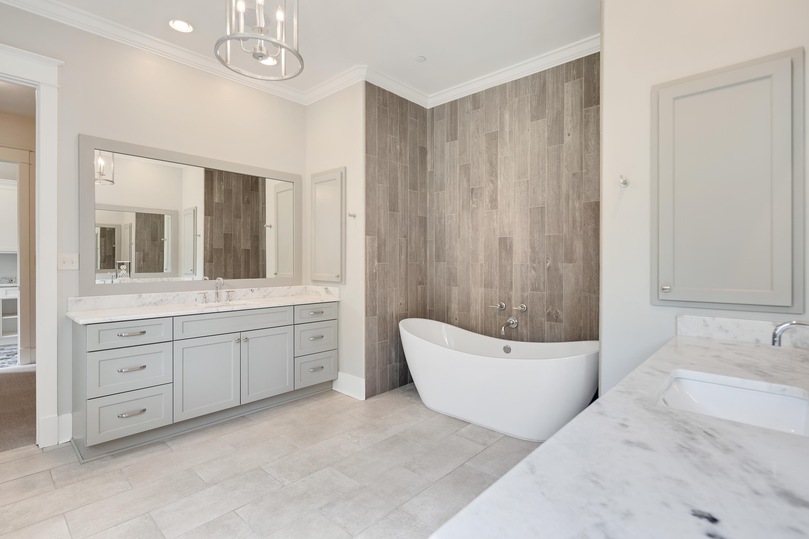 55 East Old State Line Road Piperton, TN 38017 - Photo 24 of 40 Freestanding soaking tub with wood-finish tile surround, dual vanity with light gray cabinetry, and white stone countertops