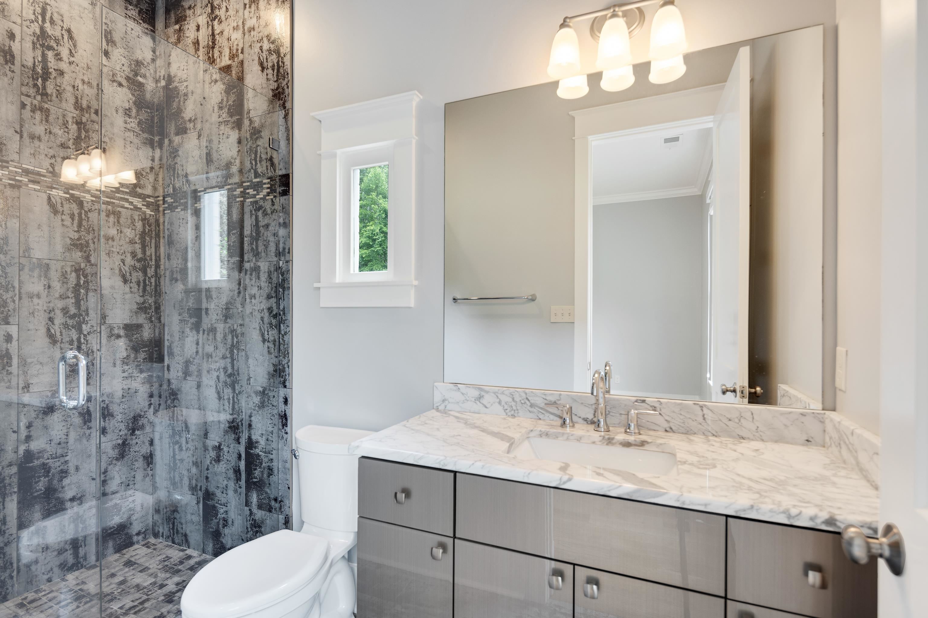 55 East Old State Line Road Piperton, TN 38017 - Photo 28 of 40 Bathroom featuring a glass-enclosed shower with textured wall tile, a window, a white toilet, and a vanity with a white stone countertop, undermount sink, and brushed nickel fixtures