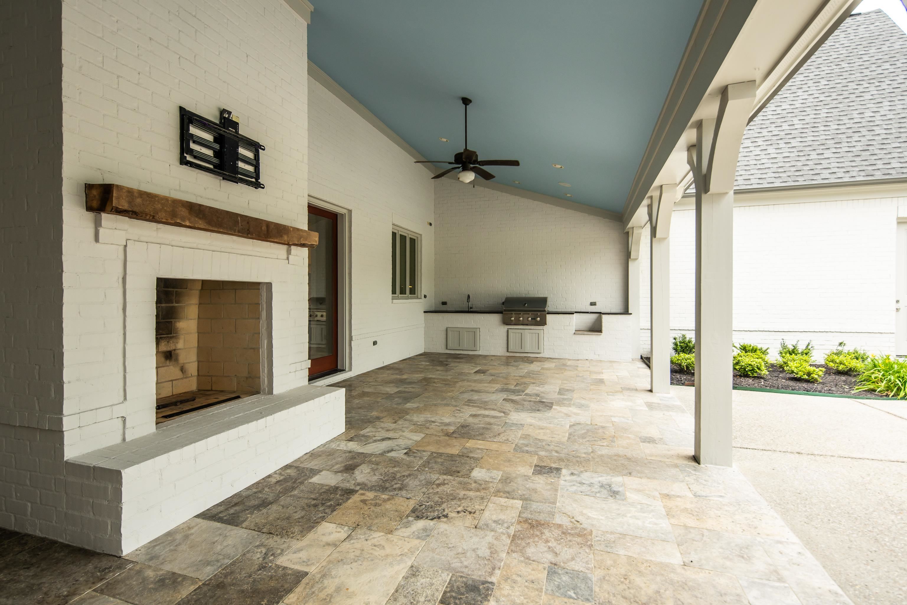55 East Old State Line Road Piperton, TN 38017 - Photo 37 of 40 Expansive covered patio featuring a white brick fireplace with a wood mantel, an outdoor kitchen with a built-in grill and sink, a ceiling fan, and large format stone tile flooring