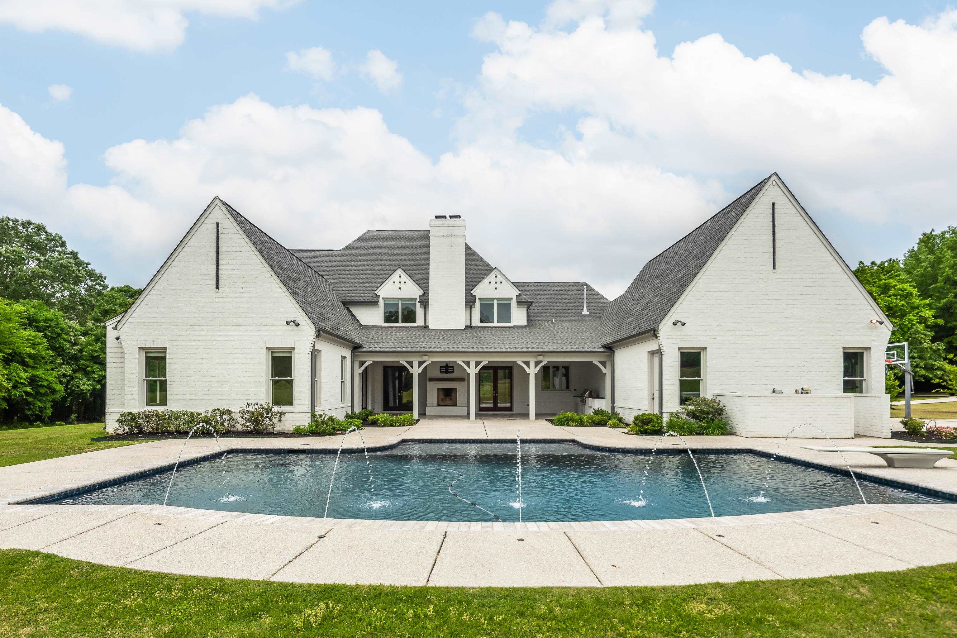 55 East Old State Line Road Piperton, TN 38017 - Photo 38 of 40 White brick exterior featuring a dark-tiled pool with water features, a spacious concrete pool deck, and a covered patio with an outdoor fireplace