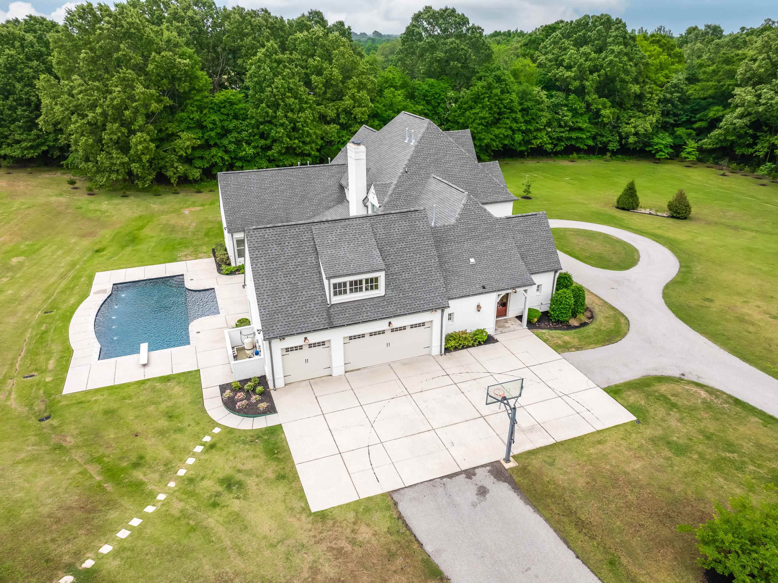 55 East Old State Line Road Piperton, TN 38017 - Photo 4 of 40 Expansive property featuring a white exterior with dark gray roofing, a multi-car garage, a swimming pool with integrated water features, and a paved driveway with a circular turnaround
