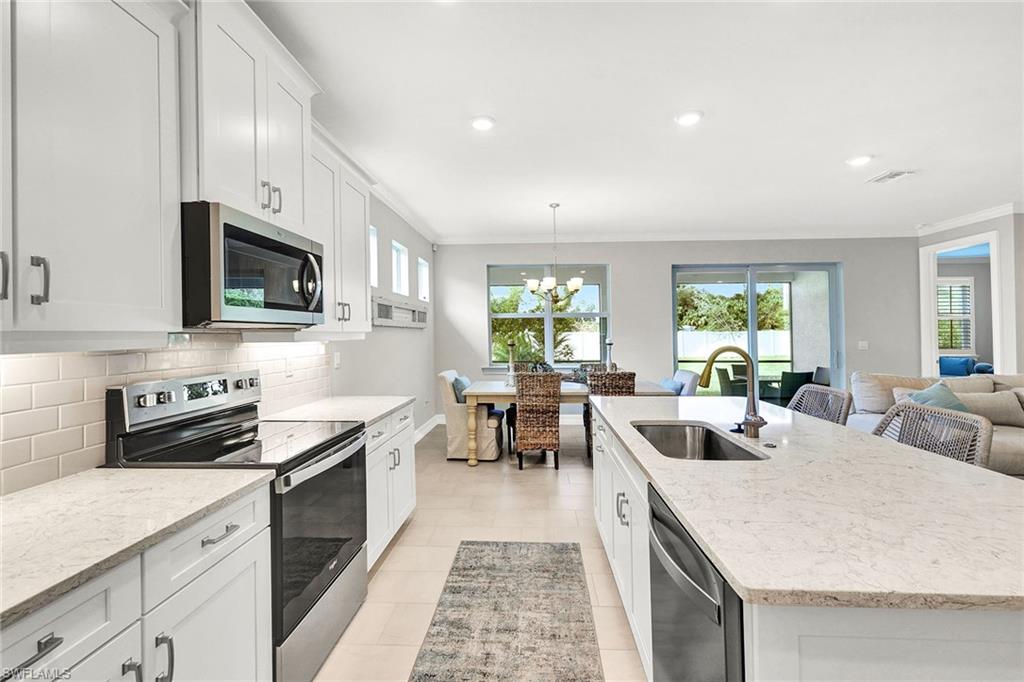 267 Tamarindo Lane Naples, FL 34114 - Photo 4 of 45 a kitchen with stainless steel appliances granite countertop a stove top oven a sink a dining table and chairs with white cabinets