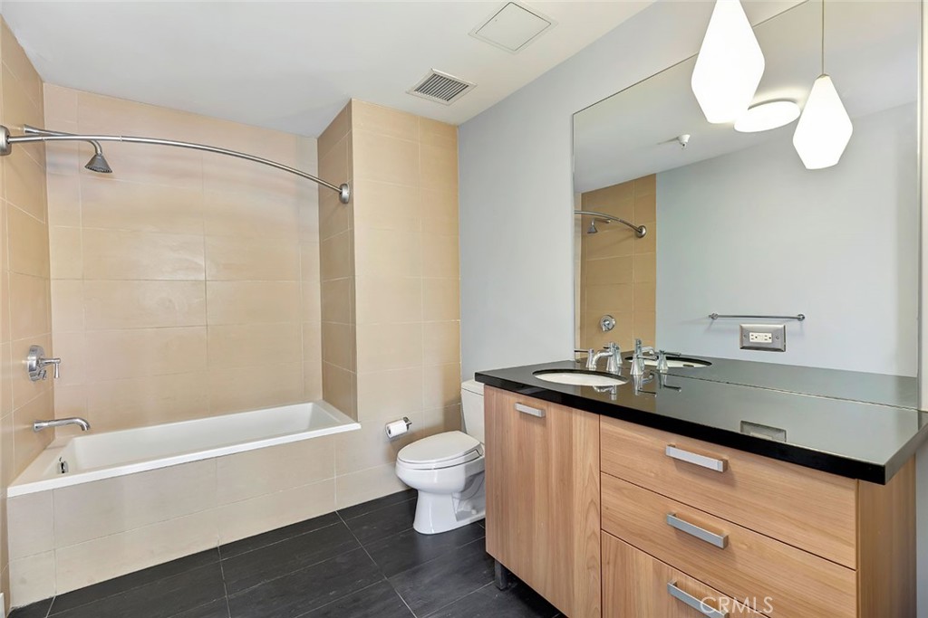 460 South Spring Street, Unit 802 Los Angeles, CA 90013 - Photo 24 of 25 a bathroom with a granite countertop sink a toilet a mirror a bathtub and shower