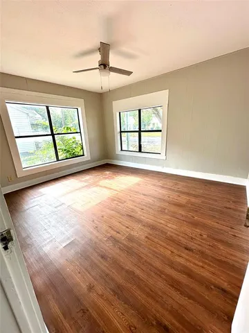 an empty room with wooden floor chandelier and windows