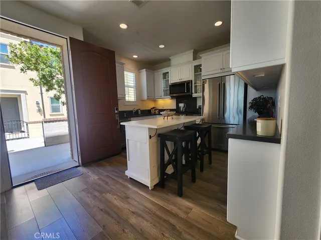 a kitchen with stainless steel appliances a stove a refrigerator a sink a dining table and chairs with wooden floor