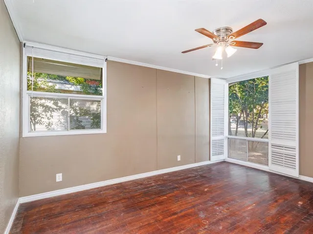 an empty room with wooden floor fan and windows