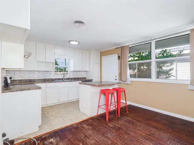 a kitchen with granite countertop a stove a sink and white cabinets with wooden floor