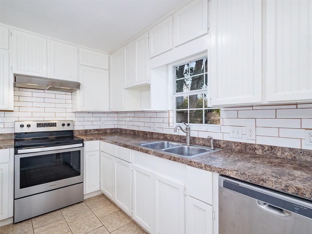 311 Miami Street Coleman, TX 76834 - Photo 9 of 31 a kitchen with granite countertop a sink stainless steel appliances white cabinets and a window