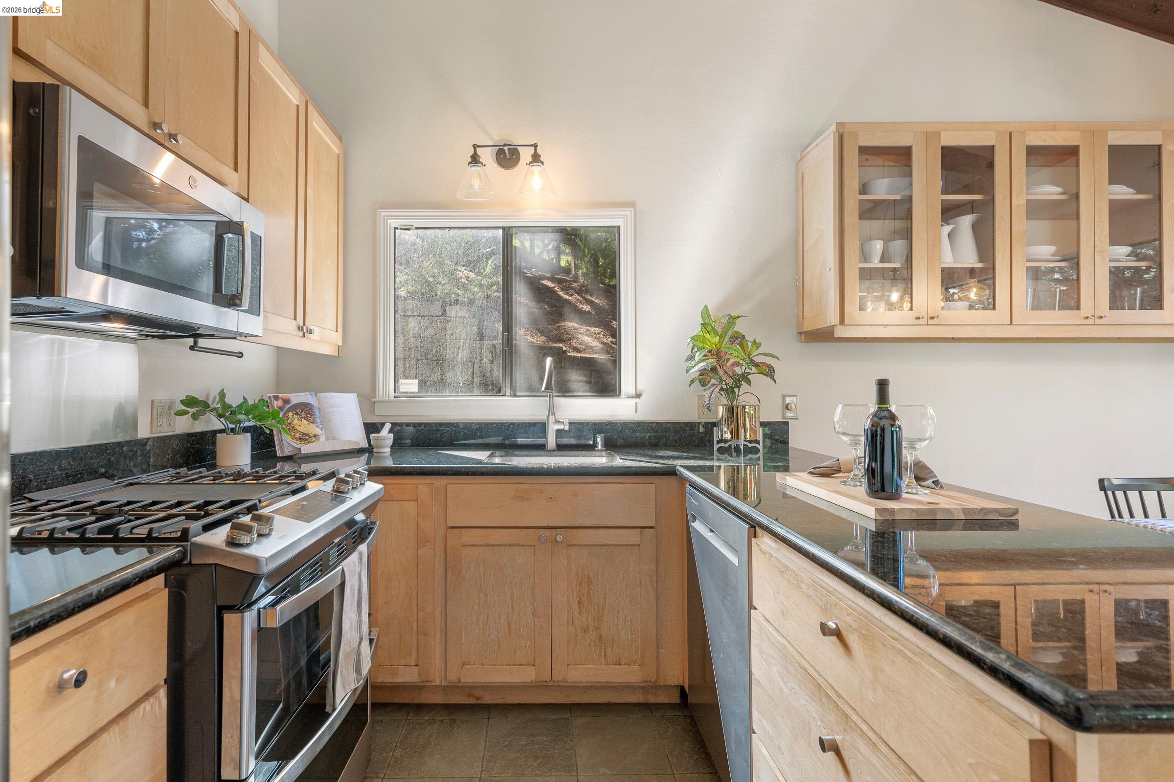 6600 Heather Ridge Way Oakland, CA 94611 - Photo 21 of 58 Kitchen with stainless steel appliances, light wood finish cabinetry, glass insert cabinets, a peninsula, and lofted ceiling