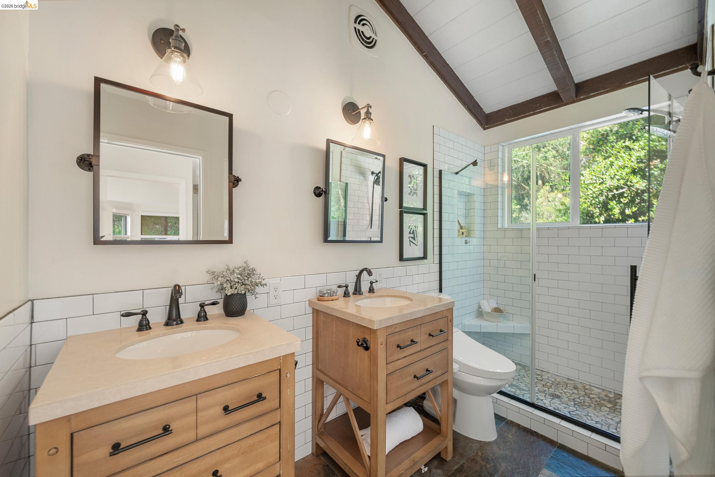6600 Heather Ridge Way Oakland, CA 94611 - Photo 36 of 58 Bathroom with tile walls, two vanities, a stall shower, a wainscoted wall, and lofted ceiling