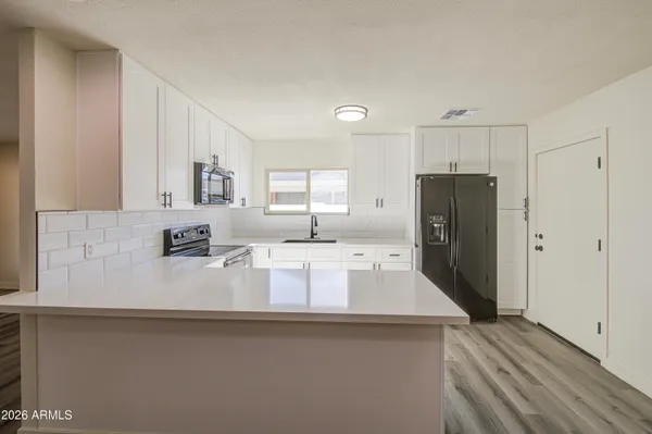 a large kitchen with stainless steel appliances a refrigerator a sink a stove and white cabinets with wooden floor