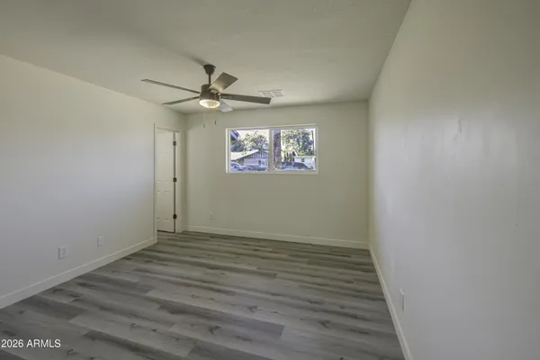 an empty room with wooden floor ceiling fan and windows