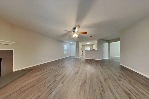a view of an empty room with wooden floor and a ceiling fan