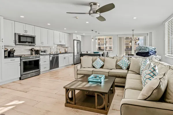a living room with stainless steel appliances kitchen island granite countertop a stove a sink a refrigerator a stove a dining table and chairs with wooden floor