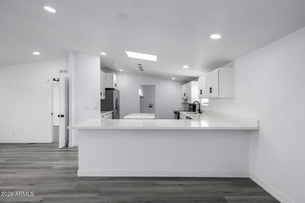 a large white kitchen with kitchen island a sink a stove a refrigerator and white cabinets with wooden floor