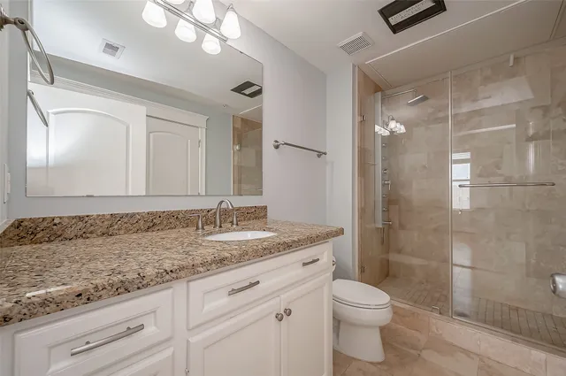a bathroom with a granite countertop sink a toilet a mirror and shower