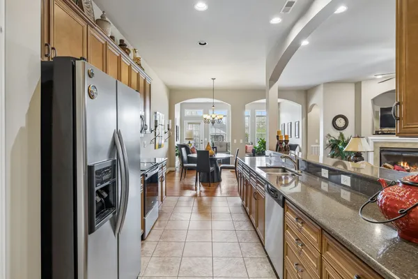 a kitchen with stainless steel appliances granite countertop a refrigerator a sink dishwasher a stove and a dining table with wooden floor