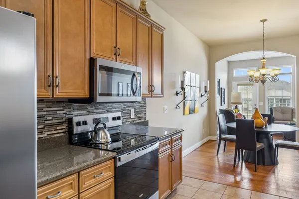 a kitchen with stainless steel appliances granite countertop a stove top oven a sink a dining table and chairs with wooden floor