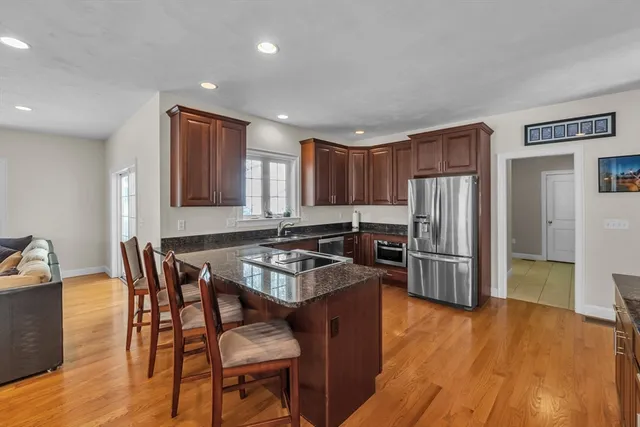 a kitchen with stainless steel appliances granite countertop a stove a refrigerator a sink a dining table and chairs with wooden floor