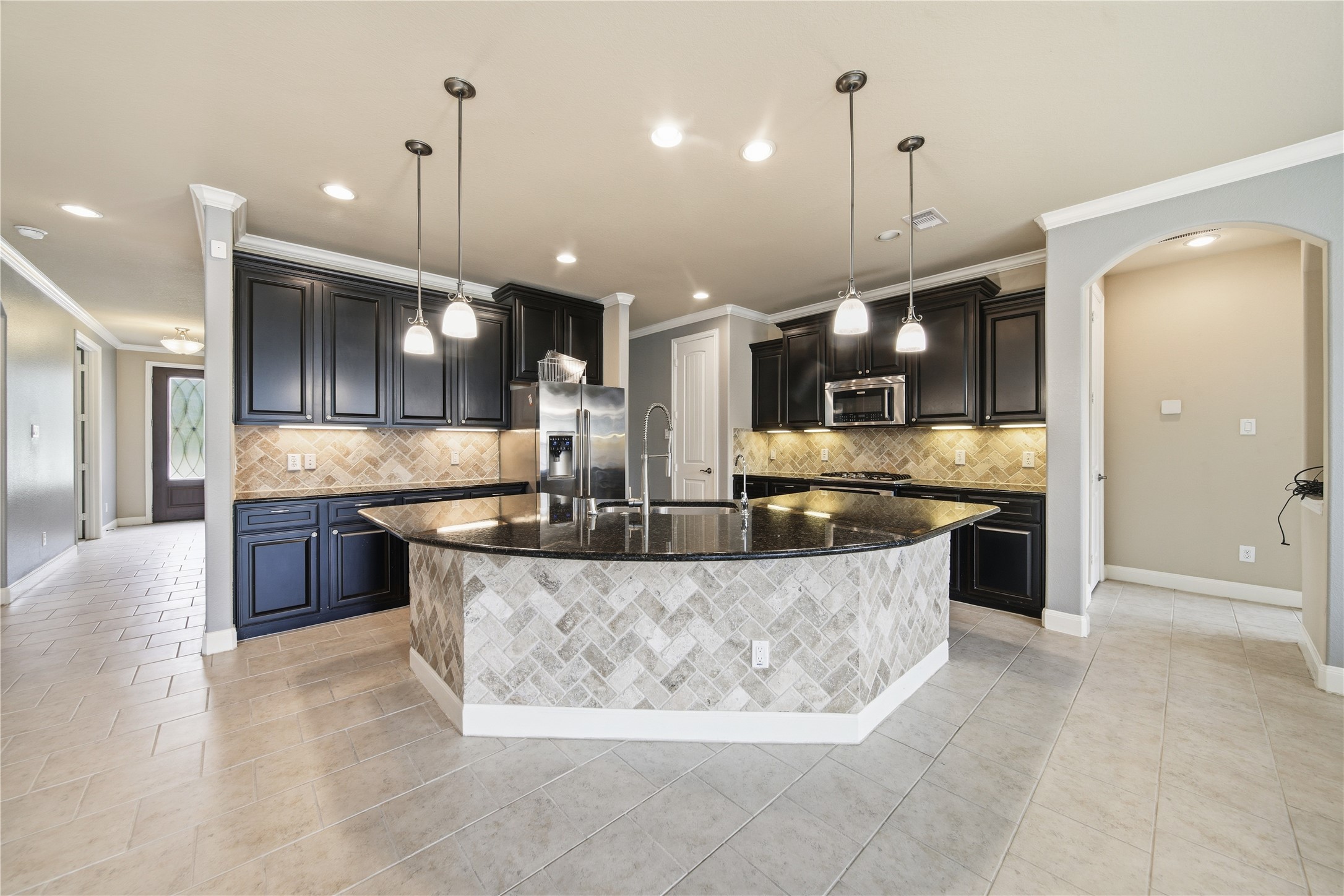 5303 Mesquite Willow Lane Rosharon, TX 77583 - Photo 4 of 32 This modern kitchen features dark cabinetry, a large central island with a granite countertop, and pendant lighting. Stainless steel appliances and a patterned tile backsplash add a stylish touch, while the open layout offers ample space for cooking and entertaining.