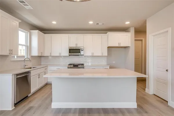 a large kitchen with stainless steel appliances granite countertop a stove a sink a refrigerator and white cabinets with wooden floor