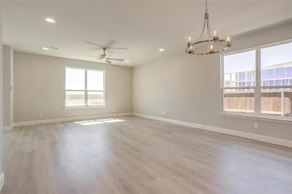 an empty room with wooden floor chandelier and windows