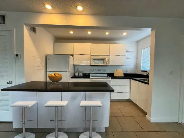 a kitchen with stainless steel appliances granite countertop a stove a sink a refrigerator and white cabinets with wooden floor