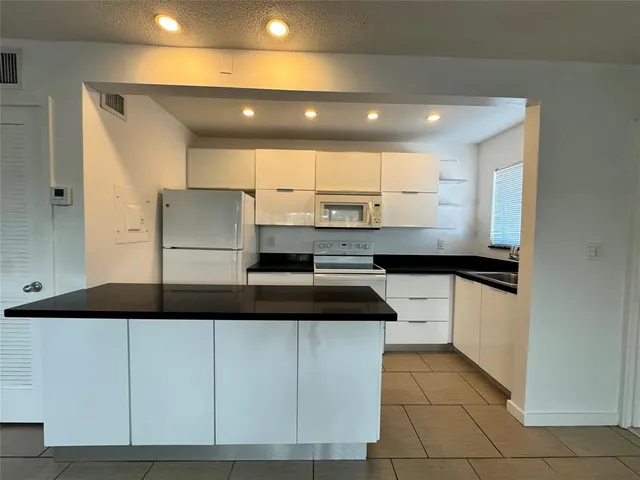 a kitchen with kitchen island granite countertop a sink a stove a refrigerator and white cabinets