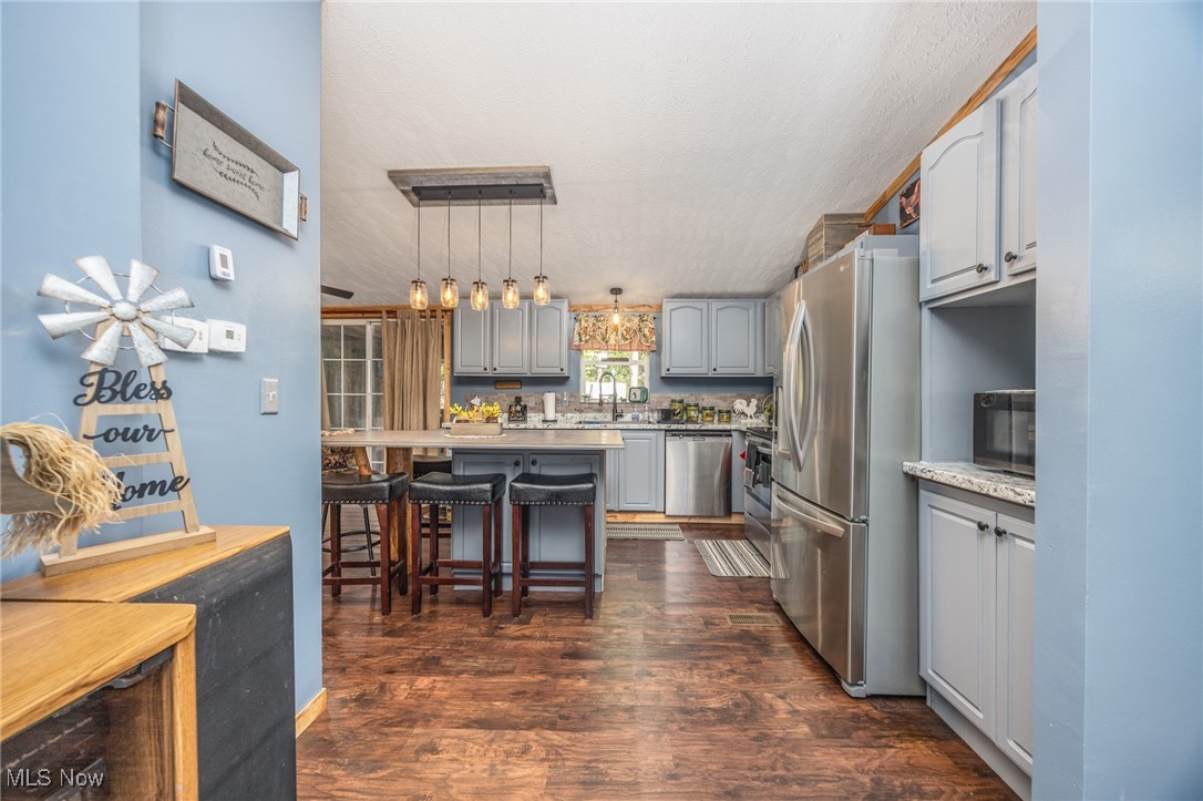 1788 Rosenbush Road Newport, OH 45768 - Photo 15 of 34 Kitchen featuring a breakfast bar, gray cabinetry, appliances with stainless steel finishes, dark wood-style flooring, and pendant lighting