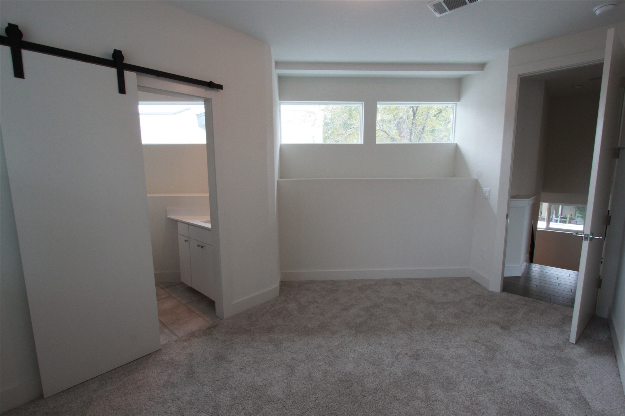 1204 Cometa Street, Unit A Austin, TX 78721 - Photo 27 of 38 Unfurnished bedroom with multiple windows, light colored carpet, and a barn door