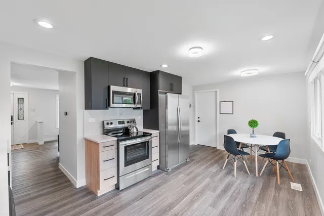 a kitchen with stainless steel appliances a dining table chairs stove refrigerator and wooden floor