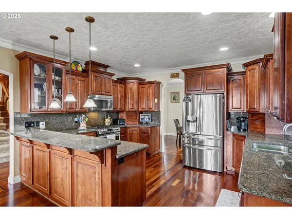 a kitchen with stainless steel appliances granite countertop a refrigerator a sink dishwasher a stove and white countertops with wooden floor