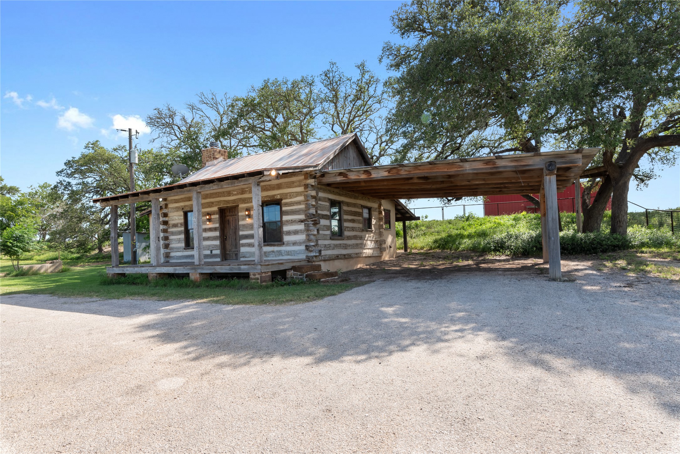 125 Hye Albert Road Hye, TX 78635 - Photo 27 of 39 Log-style house featuring a metal roof, driveway, covered porch, log siding, and a chimney
