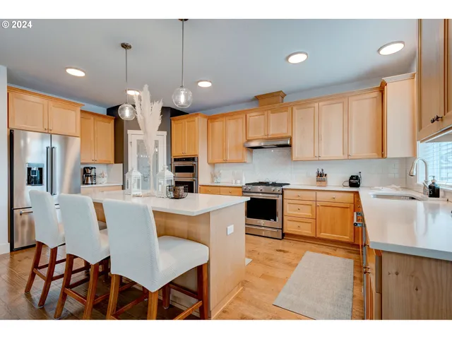 a kitchen with stainless steel appliances granite countertop a refrigerator a sink dishwasher a stove and white cabinets with wooden floor