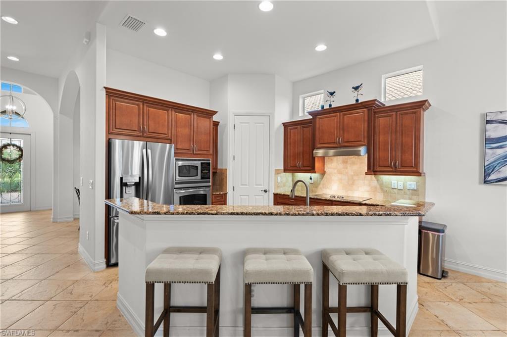 7806 Ashton Road Naples, FL 34113 - Photo 6 of 27 Kitchen with visible vents, stainless steel appliances, under cabinet range hood, a breakfast bar area, and backsplash